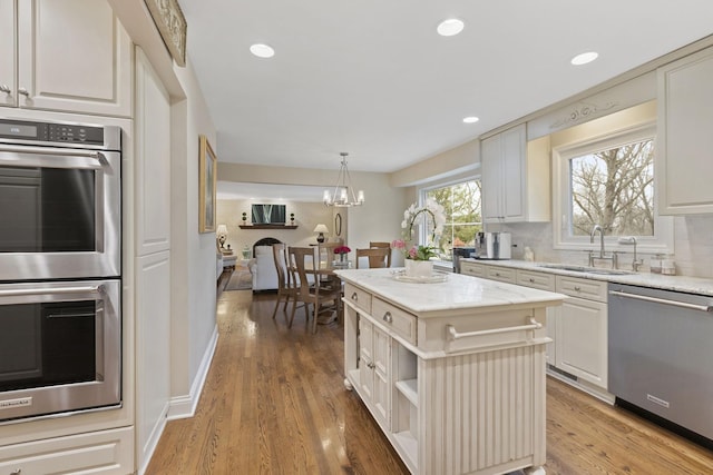 kitchen with light wood-style flooring, decorative backsplash, appliances with stainless steel finishes, a sink, and a kitchen island