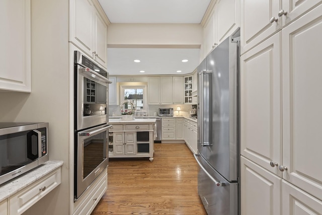 kitchen featuring a toaster, glass insert cabinets, stainless steel appliances, light wood-style floors, and recessed lighting