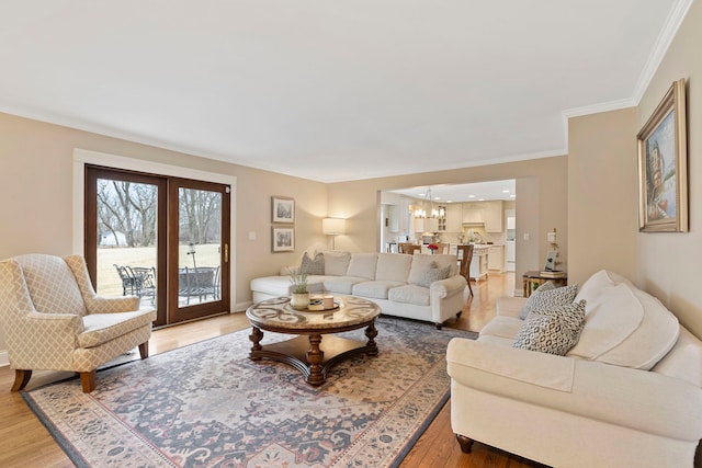 living area with light wood-type flooring, baseboards, a chandelier, and ornamental molding