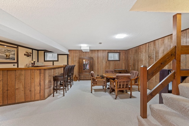 dining room with stairs, wooden walls, bar area, and light colored carpet