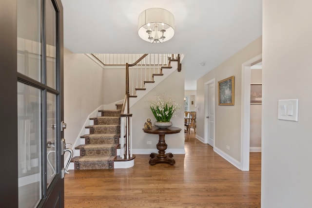 entryway with stairs, a chandelier, baseboards, and wood finished floors