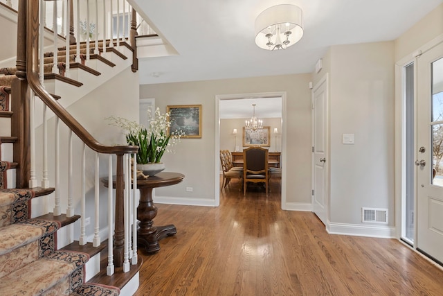 entryway featuring baseboards, visible vents, wood finished floors, an inviting chandelier, and stairs