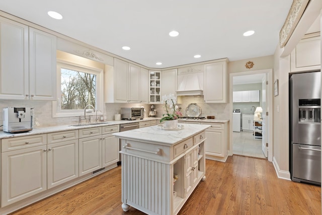 kitchen featuring light wood finished floors, appliances with stainless steel finishes, custom exhaust hood, and a sink