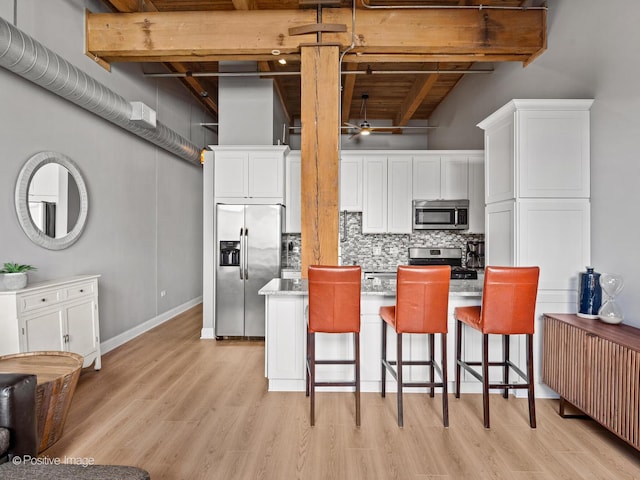 kitchen featuring a breakfast bar area, white cabinetry, appliances with stainless steel finishes, backsplash, and beamed ceiling