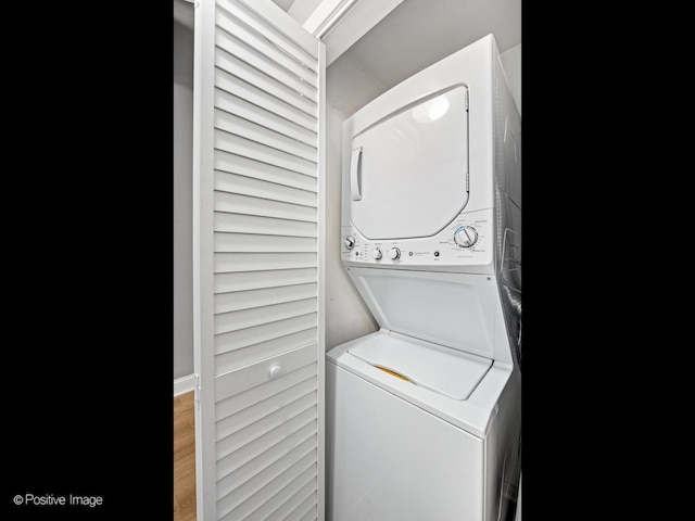 clothes washing area with laundry area, wood finished floors, and stacked washer and clothes dryer