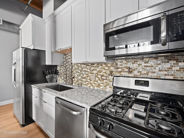 kitchen featuring stainless steel appliances, backsplash, white cabinetry, a sink, and light wood-type flooring