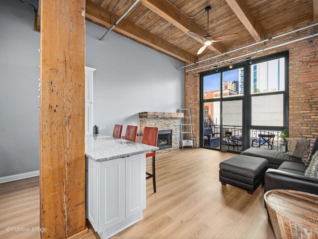 living room featuring wooden ceiling, a fireplace, a ceiling fan, light wood-style floors, and beam ceiling