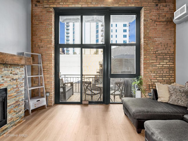 living area with expansive windows, brick wall, a stone fireplace, and wood finished floors