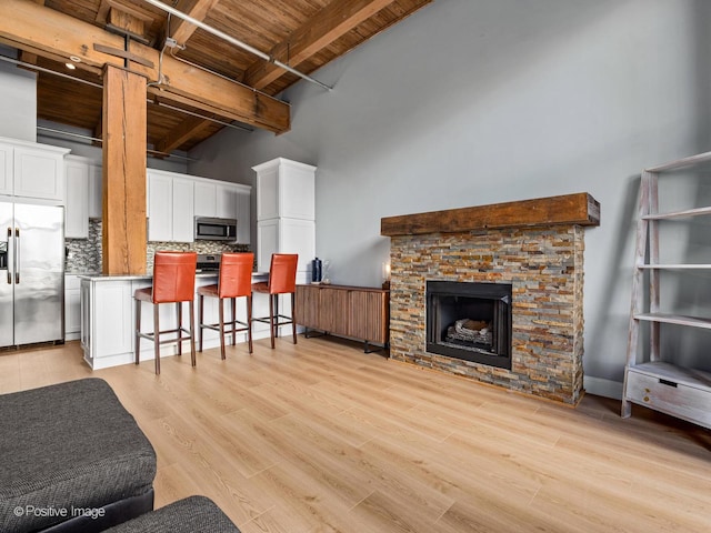 living area featuring wooden ceiling, a fireplace, a towering ceiling, light wood finished floors, and beamed ceiling