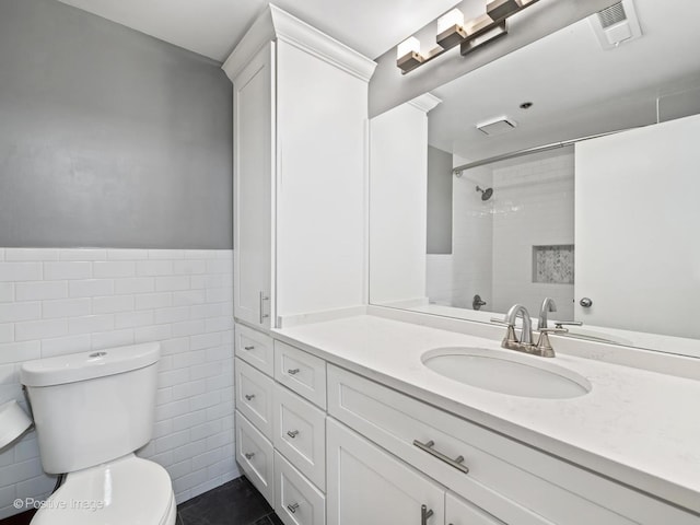 bathroom featuring tile walls, visible vents, toilet, vanity, and walk in shower