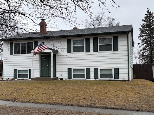 bi-level home featuring a shingled roof, a front yard, fence, and a chimney