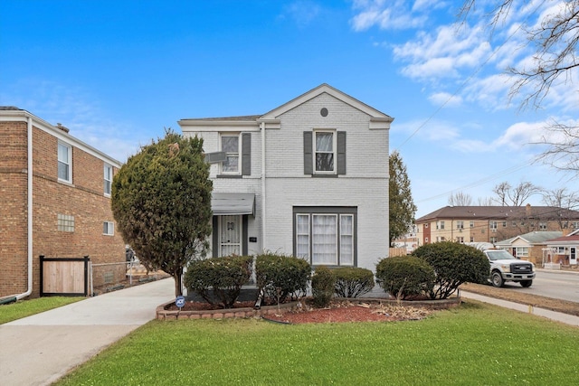 traditional home featuring a front lawn, fence, and brick siding