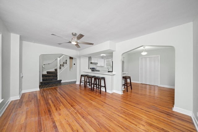 unfurnished living room featuring hardwood / wood-style floors, stairway, a ceiling fan, baseboards, and arched walkways