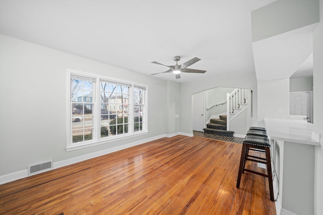 living area with hardwood / wood-style floors, a ceiling fan, baseboards, visible vents, and stairs