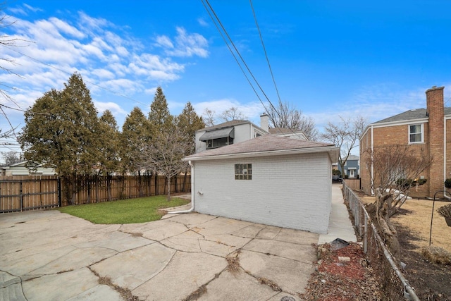 back of property featuring fence, roof with shingles, brick siding, a chimney, and a patio area