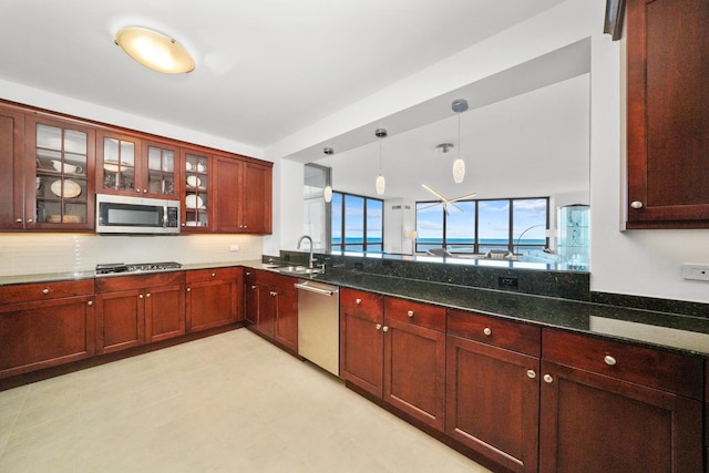 kitchen featuring reddish brown cabinets, appliances with stainless steel finishes, dark stone countertops, hanging light fixtures, and a sink