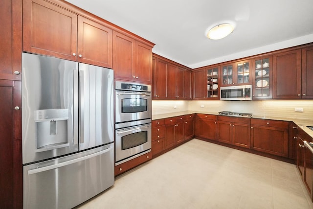 kitchen with light floors, stainless steel appliances, tasteful backsplash, light countertops, and glass insert cabinets