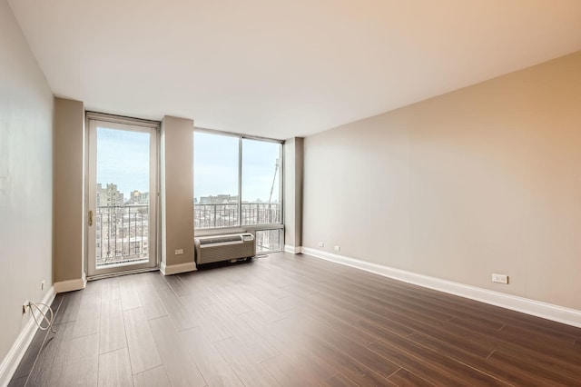 spare room featuring a wall unit AC, a city view, dark wood-style flooring, baseboards, and expansive windows