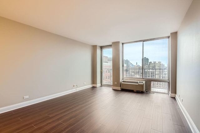 unfurnished room featuring dark wood-style flooring, a city view, expansive windows, an AC wall unit, and baseboards