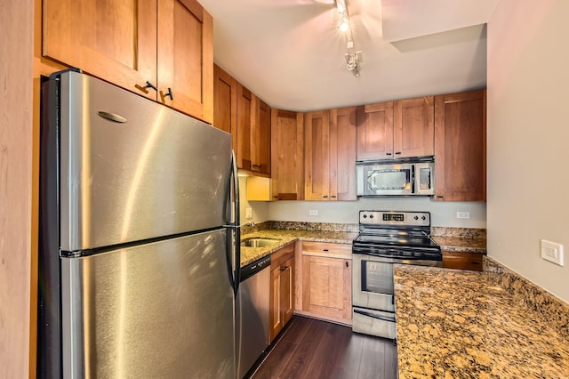 kitchen with brown cabinetry, appliances with stainless steel finishes, dark wood-type flooring, stone counters, and a sink