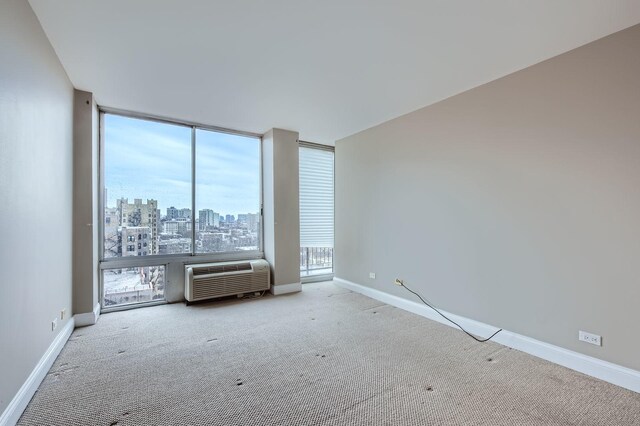 carpeted empty room with a view of city, expansive windows, a wall unit AC, and baseboards