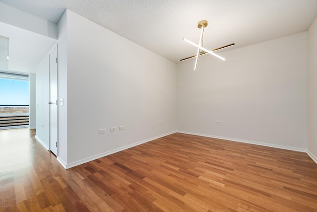 spare room with a textured ceiling, light wood-style floors, baseboards, and a chandelier