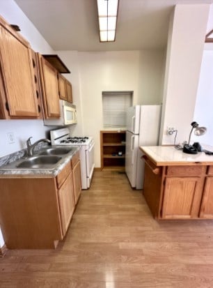 kitchen with light countertops, white appliances, a sink, and light wood-style floors