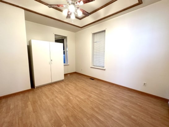 unfurnished bedroom with a tray ceiling, visible vents, light wood-style flooring, and baseboards