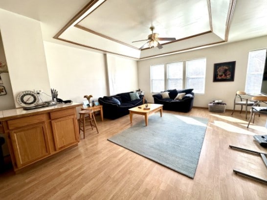 living area featuring light wood-type flooring, a tray ceiling, and a ceiling fan