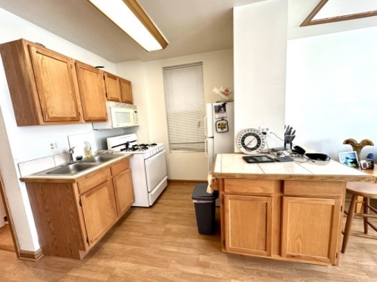 kitchen with white appliances, tile countertops, a breakfast bar, light wood-type flooring, and a sink