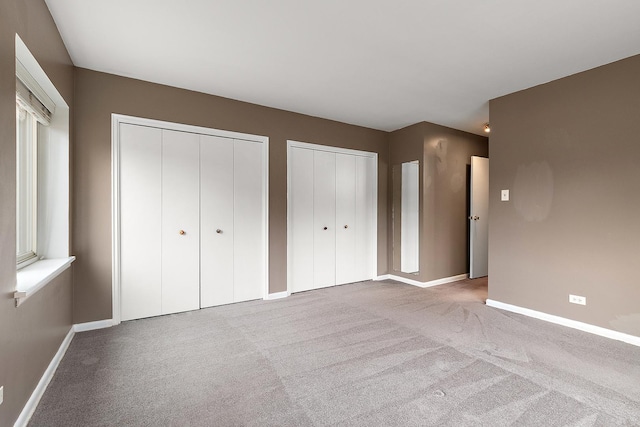 unfurnished bedroom with multiple closets, carpet, and baseboards