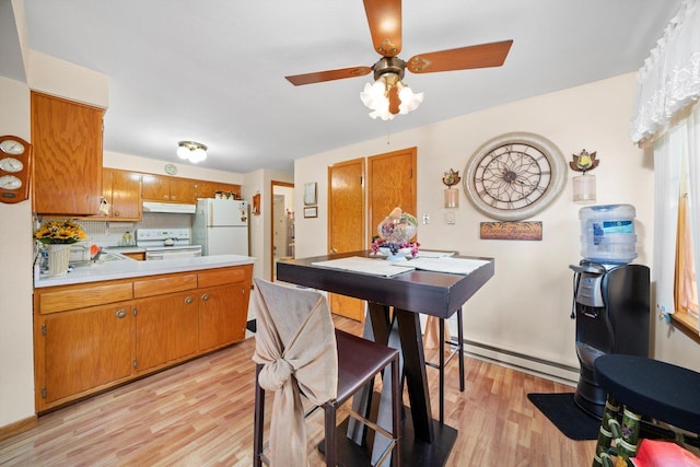 kitchen with white appliances, brown cabinetry, baseboard heating, light countertops, and under cabinet range hood