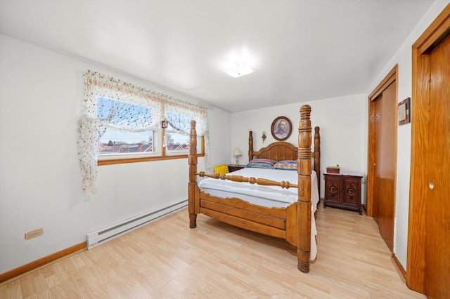 bedroom with a baseboard heating unit, a closet, light wood-style floors, and baseboards