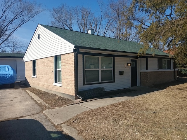 view of front of home with driveway, a shingled roof, a chimney, and brick siding