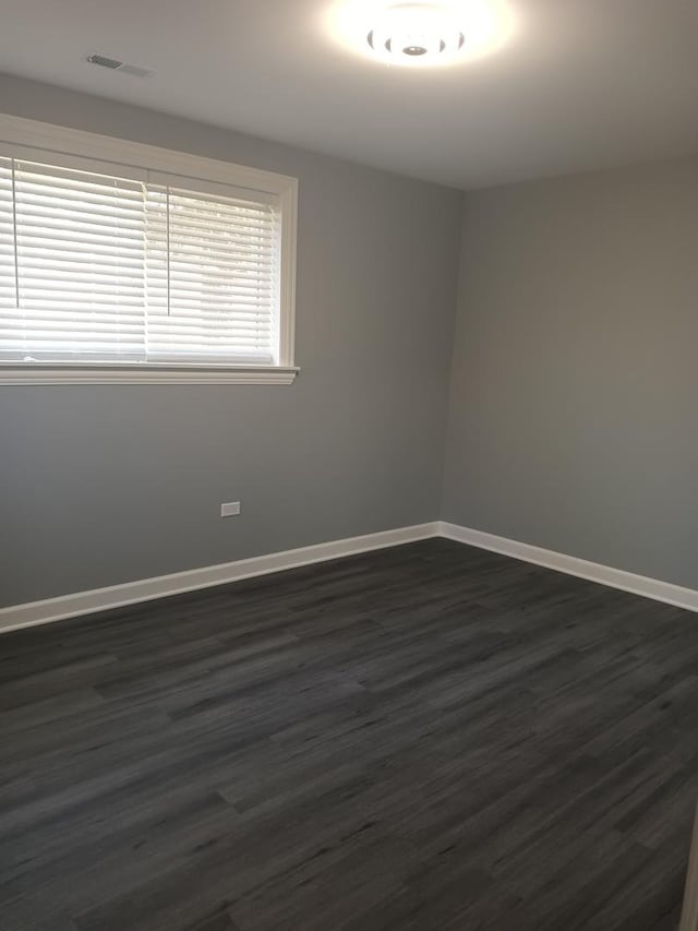 unfurnished room with dark wood-type flooring, visible vents, and baseboards