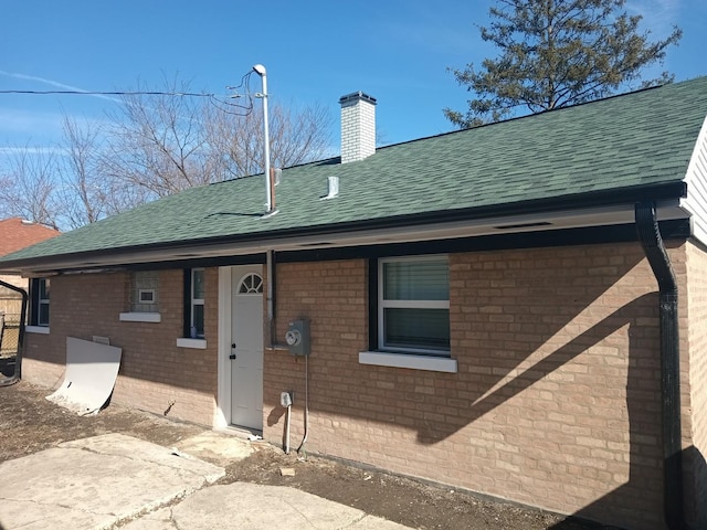 view of front facade featuring a shingled roof, brick siding, and a chimney