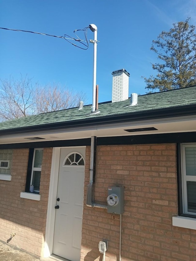 entrance to property with roof with shingles, a chimney, and brick siding