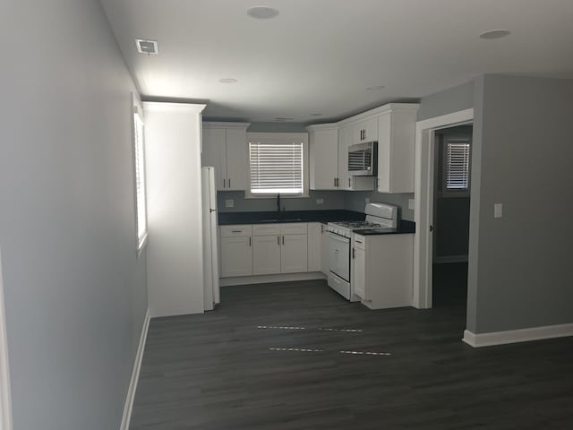 kitchen featuring white appliances, a sink, visible vents, white cabinetry, and dark countertops