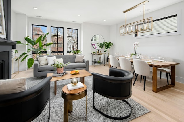 living area with light wood finished floors, baseboards, a glass covered fireplace, a notable chandelier, and recessed lighting