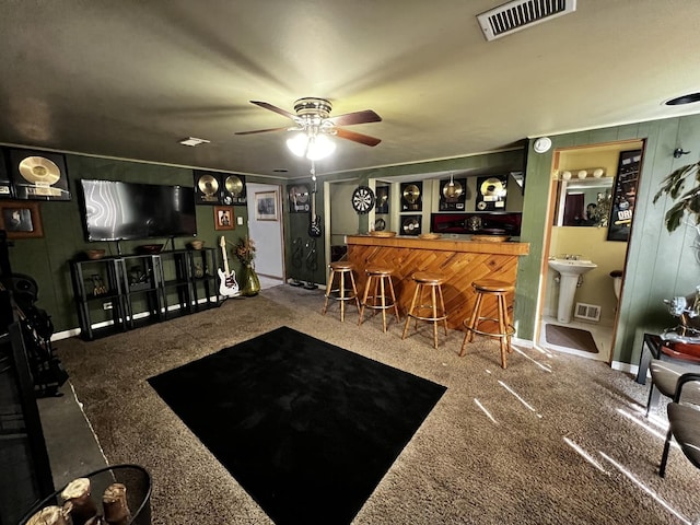 carpeted living room featuring a bar, a ceiling fan, visible vents, and a sink