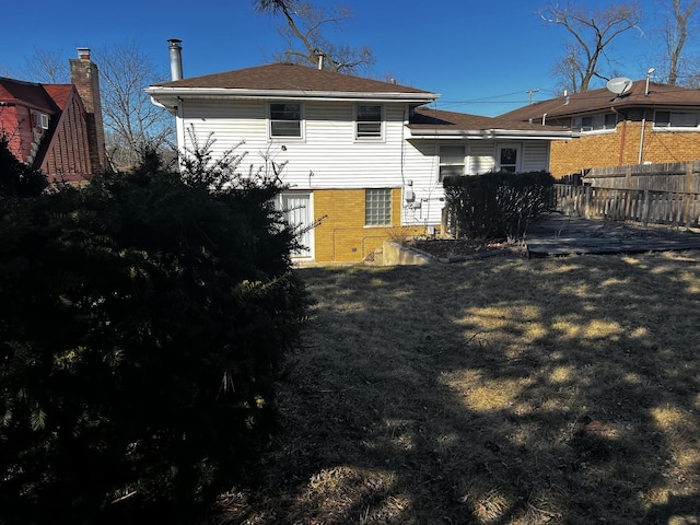 back of house featuring brick siding, a lawn, and fence