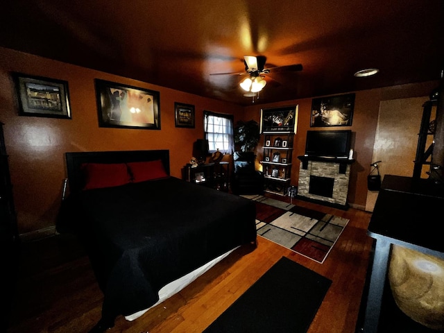 bedroom featuring a fireplace, a ceiling fan, and wood finished floors