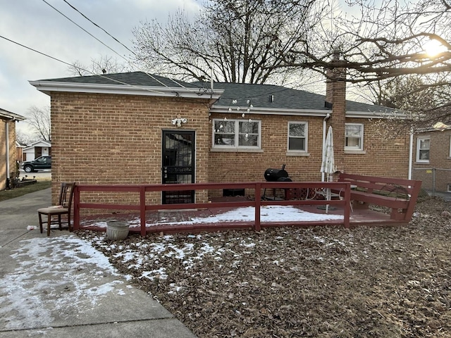 snow covered back of property with a shingled roof and brick siding