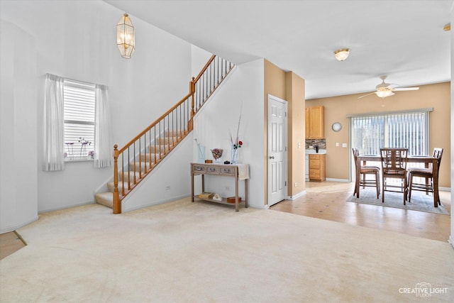 living area featuring ceiling fan, stairway, and light colored carpet