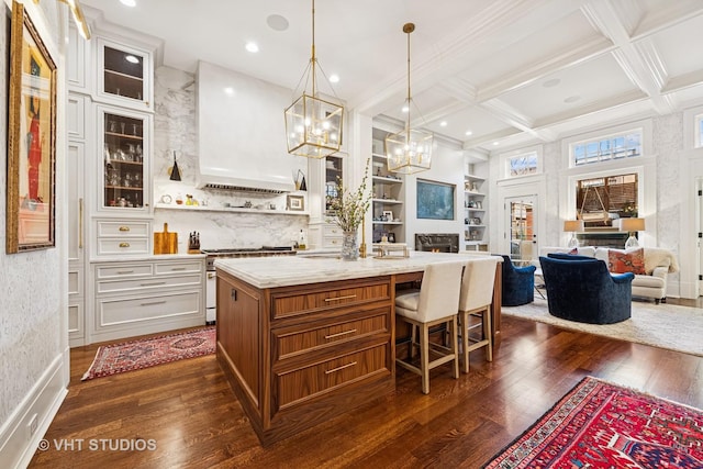 kitchen with high end stove, an island with sink, custom exhaust hood, coffered ceiling, and open shelves