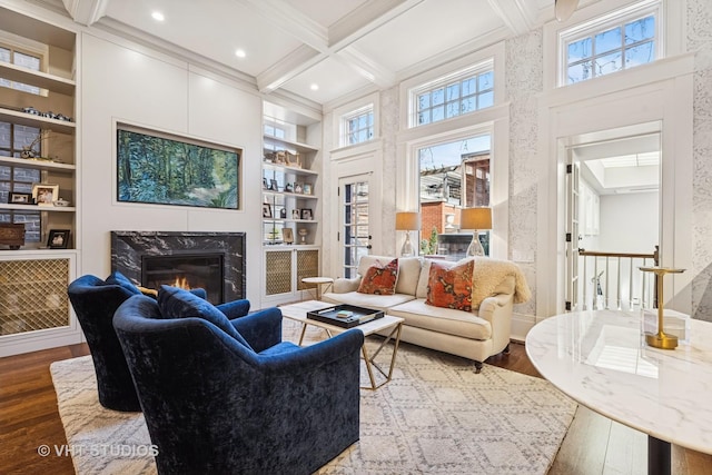 living room with beam ceiling, built in features, coffered ceiling, hardwood / wood-style floors, and a premium fireplace