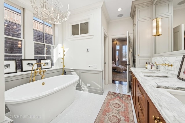 ensuite bathroom with a wainscoted wall, crown molding, a decorative wall, and an inviting chandelier