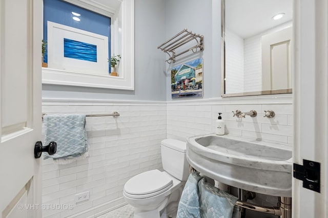 half bath featuring recessed lighting, a sink, wainscoting, tile walls, and toilet