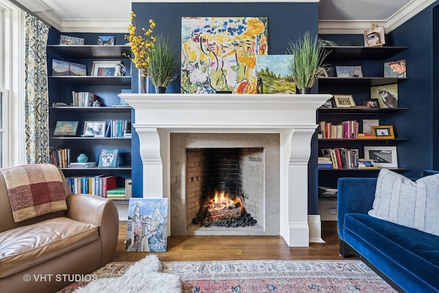 sitting room with a warm lit fireplace, wood finished floors, and ornamental molding