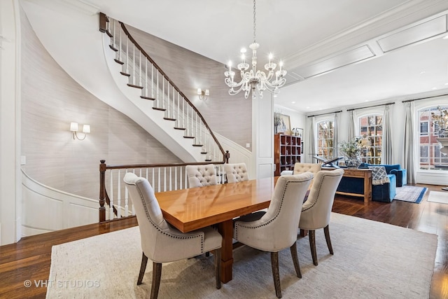 dining room with wood finished floors, wainscoting, crown molding, a decorative wall, and a chandelier